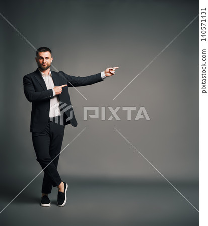 Stylish man in black suit pointing hands at grey copy space Stylish man in black suit pointing hands at grey copy space 140571431
