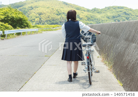 一名高中女生推著自行車走路。 140571458