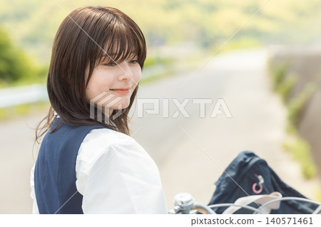 A high school girl in uniform gently turns around while pushing her bicycle. A high school girl in uniform gently turns around while pushing her bicycle. 140571461