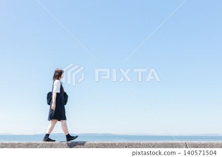 一名身穿校服的高中女生,以藍天碧海為背景,向前走。 一名身穿校服的高中女生,以藍天碧海為背景,向前走。 140571504