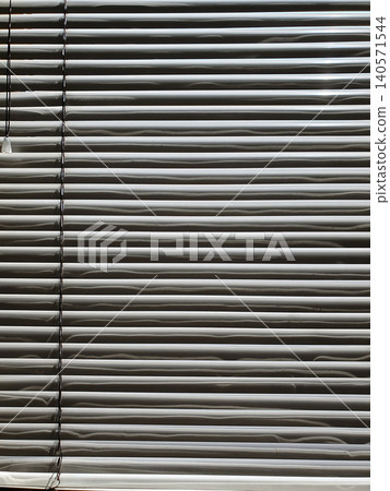 White horizontal blinds on a window close-up. Play of light and shadow, minimalist pattern and geometric texture White horizontal blinds on a window close-up. Play of light and shadow, minimalist pattern and geometric texture 140571544