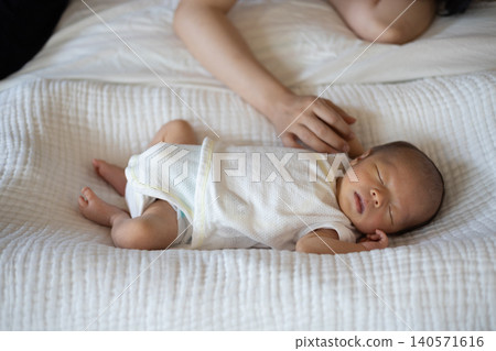 A sleeping baby (newborn) and the mother's hands as she soothes it. A sleeping baby (newborn) and the mother's hands as she soothes it. 140571616