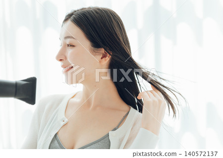 A young woman drying her wet hair with a hairdryer. 140572137