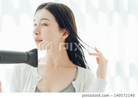 A young woman drying her wet hair with a hairdryer. 140572140
