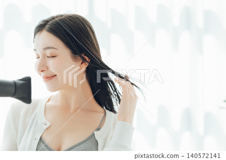 A young woman drying her wet hair with a hairdryer. A young woman drying her wet hair with a hairdryer. 140572141