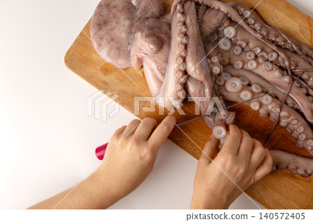 Hands preparing fresh raw octopus on a rustic wooden cutting board, cleaning tentacles with a knife for cooking a delicious seafood dish with traditional flavors Hands preparing fresh raw octopus on a rustic wooden cutting board, cleaning tentacles with a knife for cooking a delicious seafood dish with traditional flavors 140572405