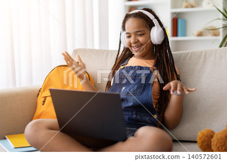 Black teenage girl participating in online video call using laptop and headphones Black teenage girl participating in online video call using laptop and headphones 140572601