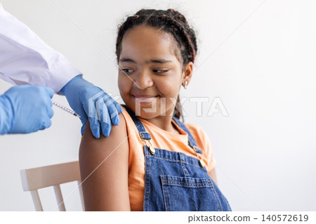 Black teenage girl receiving vaccine injection from healthcare professional in blue gloves Black teenage girl receiving vaccine injection from healthcare professional in blue gloves 140572619