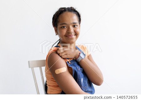 Black teenage girl demonstrating bandage on her upper arm after vaccination Black teenage girl demonstrating bandage on her upper arm after vaccination 140572655