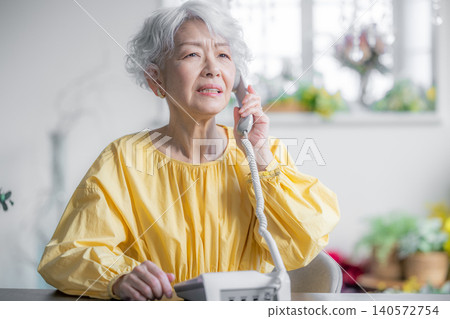 A senior woman making a phone call on a landline. A senior woman making a phone call on a landline. 140572754
