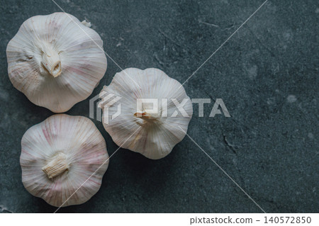 Studio close up of three whole raw garlic bulbs arranged beautifully on a dark textured background, highlighting natural organic health benefits and superfood nutrition Studio close up of three whole raw garlic bulbs arranged beautifully on a dark textured background, highlighting natural organic health benefits and superfood nutrition 140572850