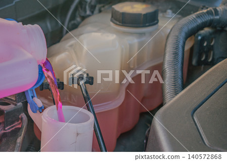 Bright pink washer fluid pouring from a plastic canister into the vertical reservoir tank neck under an open car hood during regular automotive maintenance service Bright pink washer fluid pouring from a plastic canister into the vertical reservoir tank neck under an open car hood during regular automotive maintenance service 140572868