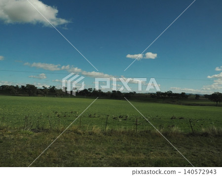 A tranquil landscape of sprawling green meadows—a peaceful land where blue skies and trees harmonize. 140572943