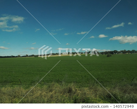 The scenery outside the train window is a continuous stretch of green grassland—a tranquil rural landscape painted by trees in the distance. 140572949