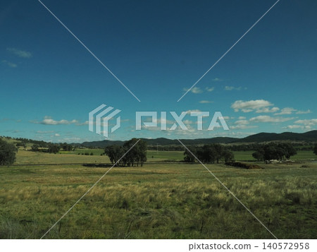 The scenery outside the train window shows small structures scattered across a grassy field—a tranquil expanse of rural landscape continues. 140572958