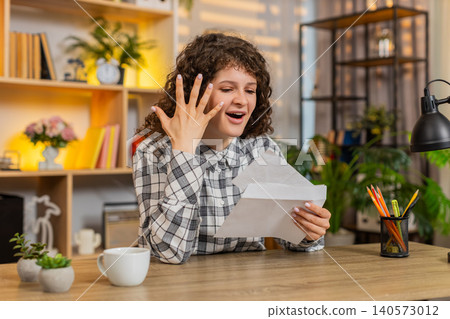 Young woman on home table reading letter with joyful reaction after positive official document news Young woman on home table reading letter with joyful reaction after positive official document news 140573012