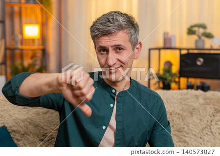 Young man shows thumbs down gesture with serious expression showing disapproval or disagreement Young man shows thumbs down gesture with serious expression showing disapproval or disagreement 140573027