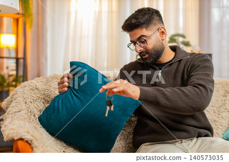 Indian man searching for apartment keys with anxious face on sofa at home, finds them with relief 140573035