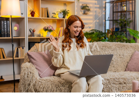 Young woman on home sofa greeting during laptop video call and speaking on friendly online meeting 140573036