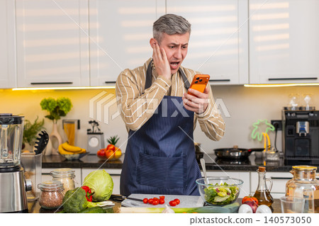 Middle-aged man shocked by smartphone message while making fresh vegetable salad in kitchen at home Middle-aged man shocked by smartphone message while making fresh vegetable salad in kitchen at home 140573050
