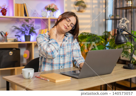 Young woman on home table working on laptop with neck pain fatigue during remote work in living room Young woman on home table working on laptop with neck pain fatigue during remote work in living room 140573057