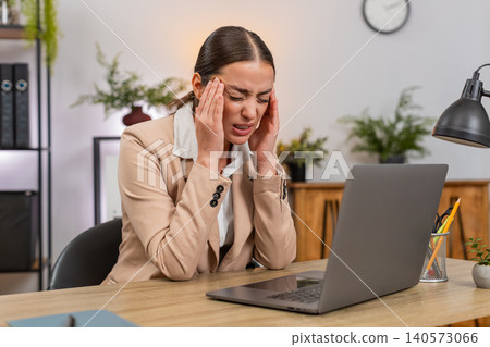 Young businesswoman rubs temples from headache while working on laptop slows down and takes breath Young businesswoman rubs temples from headache while working on laptop slows down and takes breath 140573066