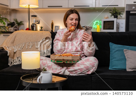 Adult woman eats pizza and messages friend on smartphone at night smiles cozy vibe social chat happy Adult woman eats pizza and messages friend on smartphone at night smiles cozy vibe social chat happy 140573110