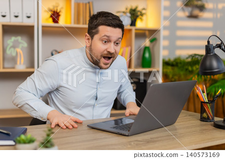 Young man on home table staring at laptop in shock with open mouth after astonishing breaking news Young man on home table staring at laptop in shock with open mouth after astonishing breaking news 140573169