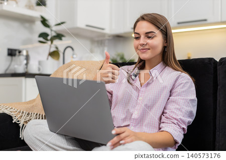 Young woman blogger waves to laptop webcam says hello show thumb up sign listens asks chat questions Young woman blogger waves to laptop webcam says hello show thumb up sign listens asks chat questions 140573176