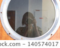 A woman holding a camera is reflected in the round window of a ship. 140574017