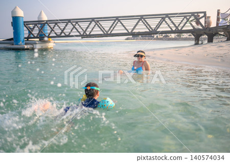 Asian woman relaxing in shallow water with her multiracial son s Asian woman relaxing in shallow water with her multiracial son s 140574034