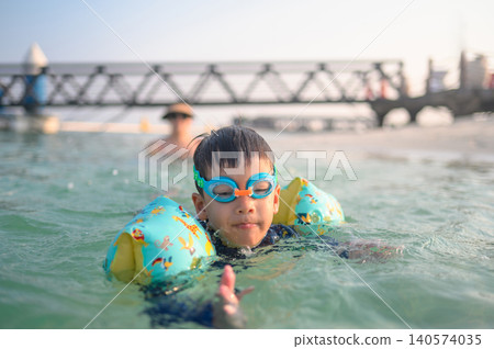 Playful Child Swimming in Shallow Water with Inflatable Arm Floaties Playful Child Swimming in Shallow Water with Inflatable Arm Floaties 140574035
