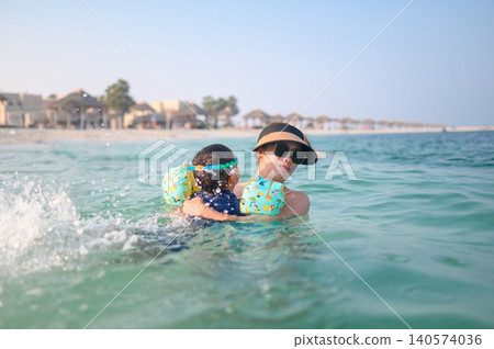 Asian woman in sunglasses carries multiracial son in water at be Asian woman in sunglasses carries multiracial son in water at be 140574036
