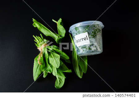 Green sorrel herb bunch with plastic container on black background Green sorrel herb bunch with plastic container on black background 140574401
