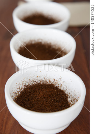ground coffee in white ceramic bowls arranged in a row on a table for specialty coffee quality testing by Q grader. Coffee cupping, tasting and grading concept in a roastery or cafe. Selective focus. ground coffee in white ceramic bowls arranged in a row on a table for specialty coffee quality testing by Q grader. Coffee cupping, tasting and grading concept in a roastery or cafe. Selective focus. 140574523