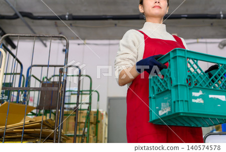 A woman carrying a container in a warehouse A woman carrying a container in a warehouse 140574578