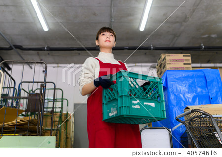 Female worker carrying a container in a warehouse 140574616