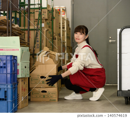 A woman sorting cardboard boxes in a warehouse. A woman sorting cardboard boxes in a warehouse. 140574619