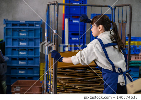 A woman working in a warehouse, moving a hand truck. A woman working in a warehouse, moving a hand truck. 140574633