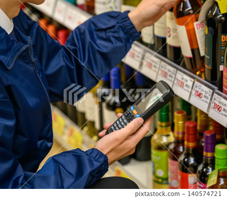 一名男子從貨架上取下一瓶葡萄酒，然後操作終端。 140574721