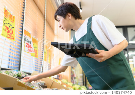 A male store clerk operating a terminal at a supermarket. A male store clerk operating a terminal at a supermarket. 140574740
