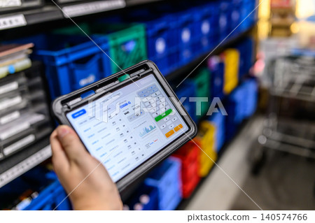 A hand holding an ordering terminal in front of the warehouse shelves. A hand holding an ordering terminal in front of the warehouse shelves. 140574766