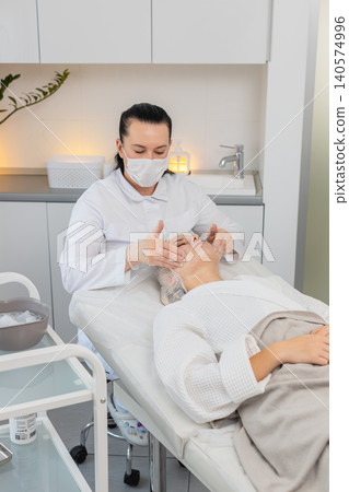 Cosmetology clinic facial peeling beautician rubbing moisturizing cream on middle aged woman skin Cosmetology clinic facial peeling beautician rubbing moisturizing cream on middle aged woman skin 140574996