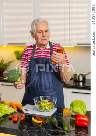 Senior old man using smartphone to check grocery list while preparing healthy meal in home kitchen 140575098