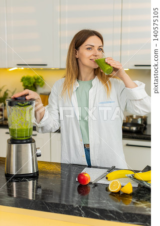 Middle-aged woman sipping green smoothie in home kitchen for healthy diet weight loss detox routine Middle-aged woman sipping green smoothie in home kitchen for healthy diet weight loss detox routine 140575105