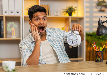Indian man on home table showing clock to camera while speaking during work in cozy home living room Indian man on home table showing clock to camera while speaking during work in cozy home living room 140575272