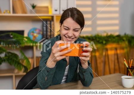 Young woman on home table winning mobile game on smartphone feeling happy during online play at desk Young woman on home table winning mobile game on smartphone feeling happy during online play at desk 140575279