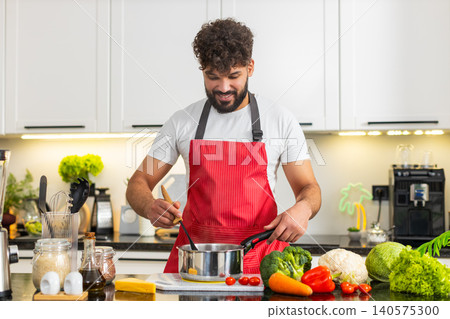 Arabian young adult man smiling stirring soup pot on stove in home kitchen for healthy dinner recipe 140575300