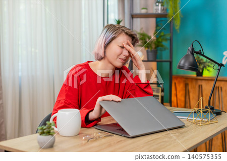 Woman tiredly closing laptop, suffering headache after long exhausting stressful remote online work Woman tiredly closing laptop, suffering headache after long exhausting stressful remote online work 140575355