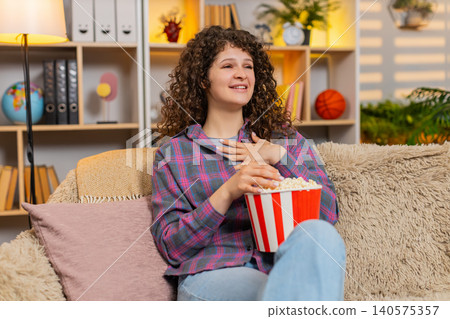 Young woman on home sofa watching fun film with popcorn laughing in surprise during home movie night Young woman on home sofa watching fun film with popcorn laughing in surprise during home movie night 140575357